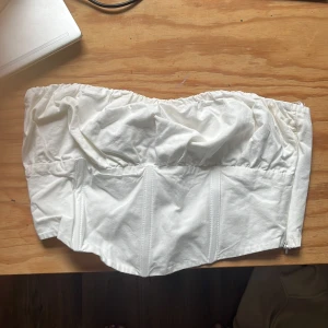 Vit korsett-topp med smock - Säljer en snygg vit korsett-topp i bomull med smockad rygg. Toppen är från Berskha i storlek M, den sitter jätte fint på och håller sig uppe väldigt bra. Använd ett fåtal gånger men är i väldigt bra skick. 