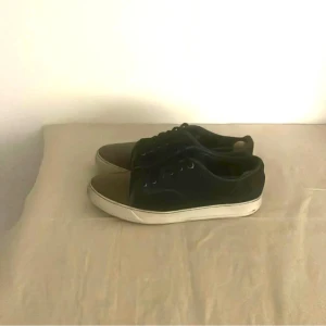 marinblå och bruna sneakers från Lanvin - Snygga sneakers från Lanvin med marinblå ovandel och bruna tår. Skorna har vita, platta sulor och klassisk snörning. Perfekta för dig som gillar stilrena och tidlösa sneakers med en twist. Passar till det mesta och ger en clean look.