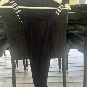 Svart ribbad baddräkt från Lindex - Cool svart baddräkt från Lindex med ribbad struktur och breda axelband med texten 'L.A. SURF'. Sitter snyggt och har en sportig vibe, perfekt för stranden eller poolen. Materialet är stretchigt och bekvämt.
