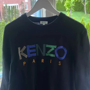 Svart Kenzo sweatshirt med broderi - Svart sweatshirt från Kenzo med färgglatt broderat logotyptryck på bröstet i blått, grönt, beige och gult. Klassisk rund halsringning och långärmad modell. Perfekt för dig som gillar streetstyle och vill sticka ut med en ikonisk tröja.