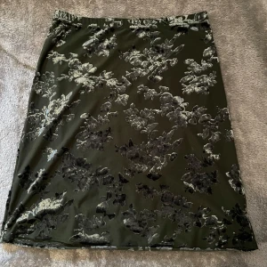 Mörkgrön sammetskjol  - Mörkgrön kjol i mjuk sammet med silvrigt blommigt mönster. Rak modell med elastisk midja och snyggt skimmer i tyget. Passar även XS/S!