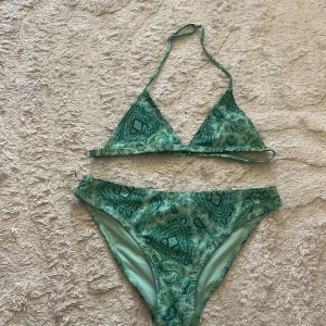 Grön paisley bikini från Gina Tricot - Snygg grön bikini från Gina Tricot med paisleyinspirerat mönster i olika gröna nyanser. Överdelen är trekantsmodell, bikinitrosan har klassisk passform. Perfekt för strandhäng och pooldagar!