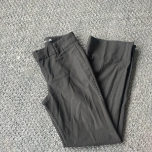 Svarta lågmidjade kostymbyxor från InWear - Klassiska svarta lågmidjade kostymbyxor från InWear med raka ben och midjehällor. Byxorna har dragkedja och hyska fram, tillverkade i ett mjukt tyg som känns dressat men ändå bekvämt. Perfekta för en clean och stilren look. Tryck ej köp nu