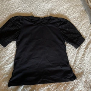 Svart blus med broderade puffärmar - Supersnygg svart blus från Reserved med puffiga, broderade ärmar och rundad hals. Ärmarna har coola håldetaljer och breda muddar som ger en unik look. Perfekt för dig som vill sticka ut lite extra med en klassisk men trendig topp.