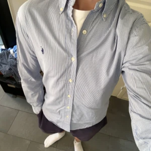 Randig Ralph Lauren Skjorta - Blå/Vit (Stl S) - Säljer denna snygga blå/vit randiga skjortan från Ralph Lauren. Skjortan är i väldigt gott skick men har två små fläckar (bild 5) som knappt syns och kan gå bort i tvätt. Nypris på skjortan ligger på ca 1600kr
