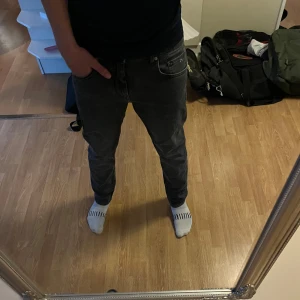 Grå jeans från J.Lindeberg - Säljer ett par grå jeans från J.Lindeberg med klassisk femficksdesign och silverfärgade detaljer. Jeansen har en slim fit passform och är tillverkade i mjukt denimtyg. Perfekta för dig som gillar stilrena och enkla byxor med snygg tvätt. Storleken är W30 L32.