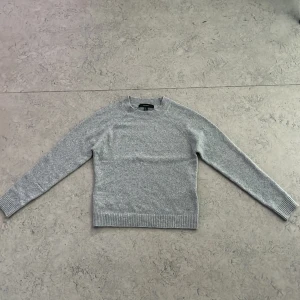 Ljusgrå stickad tröja från Vero Moda - Supermjuk och mysig ljusgrå stickad tröja från Vero Moda i storlek S. Tröjan har rund halsringning, ribbade muddar och nederkant samt lång ärm. Perfekt för lager-på-lager och enkel att matcha med jeans eller kjol.