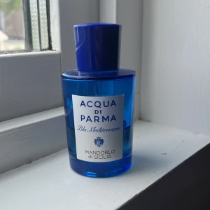 Acqua di Parma Mandorlo di Sicilia - 40 ml kvar i flaskan. Fräsch parfym i en stilren blå glasflaska från Acqua di Parma, serien Blu Mediterraneo. Doften Mandorlo di Sicilia har en elegant etikett framtill och flaskan har en rund form med matchande blått lock. Perfekt för dig som gillar exklusiva och somriga dofter.