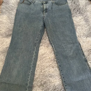 Blå bootcut jeans från Armani Jeans - Snygga blå jeans från Armani Jeans med klassisk femficksmodell och bootcut ben. Jeansen har en ljus tvätt och tydliga sömmar, samt metallknapp med logga. Perfekta för en avslappnad och stilren look.