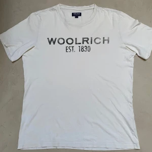 Vit Woolrich T-shirt  - Säljer nu en riktigt fet vit t-shirt från Woolrich. Den är i väldigt bra skick och är riktigt fet. Tröjan är i storlek ”M” USA och ”L” EU men jag skulle säga att den sitter som M. Texten är inte sliten utan det är ett mönster i texten. Tveka inte på att höra av er vid frågor eller funderingar.