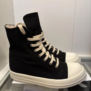 Rick owens Ramones - Snygga svarta sneakers med hög snörning och vit sula. Skorna har en rund tå och är perfekta för en stilren look. De vita skosnörena ger en fin kontrast mot det svarta tyget.