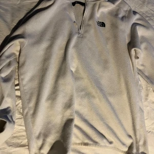 Vit fleece tröja från The North Face - Säljer en vit fleece tröja från The North Face med dragkedja vid halsen. Perfekt för kyliga dagar och outdoor-äventyr. Tröjan har långa ärmar och en klassisk passform. Hör av dig vid intresse!