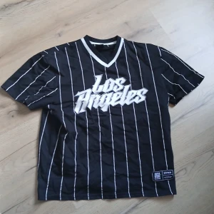 Baseballtröja  Los Angeles  - Snygg svart t-shirt med vita ränder, skick 10/10. Har använt den ett fåtal gånger och säljer den för att den inte används. Pris kan diskuteras.