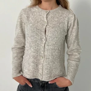 Beige/grå kofta från Design by Si - Säljer en beige kofta från Design by Si. Super söt kofta med fint stickmönster men har tyvärr aldrig kommit till användning hos mig🤍 