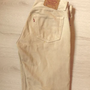 Beige Levis 501 jeans - Säljer ett par klassiska beige Levis 501 jeans. De har en knappgylf och den ikoniska raka passformen. Perfekta för en avslappnad stil.