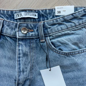 Blå jeans från Zara - Säljer ett par klassiska blå jeans från Zara med hög midja och rak passform. De har en dragkedja och knapp framtill. Perfekta för en avslappnad stil. Ordinarie pris 399