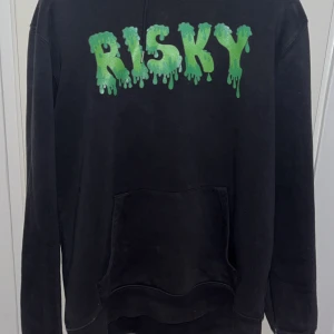 Risky universe hoodie  - Säljer en svart hoodie med en cool grön text 'RISKY' på framsidan. Hoodien har en klassisk design med långa ärmar och en bekväm huva. Perfekt för en avslappnad stil.