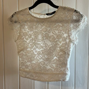 Vit spetsblus - Säljer en elegant vit spetsblus . Blusen har korta ärmar och ett vackert blommigt spetsmönster. Perfekt för en stilren look.