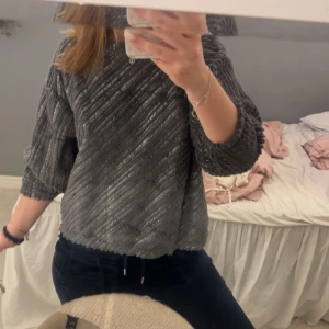 Grå glittrig tröja - Säljer en snygg grå tröja med glittrigt mönster. Tröjan har trekvartsärmar och en bekväm passform. Perfekt för att lägga till lite glitter i vardagen!