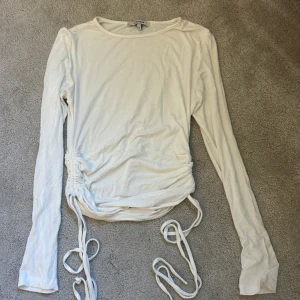 Vit långärmad topp med snörning - Säljer en stilren vit långärmad topp med snörning i midjan. Storlek s 