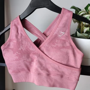 Fin rosa Gymshark sportbh i storlek S - Otroligt fin rosa kamouflage sportbh från märket Gymshark. Storlek S. Stretchig i materialet. Sportbhn har resår i nederkant och en omlott design fram. Den har även en jätte snygg criss cross design på ryggen. Snygg lite diskretare Gymsharklogga i nederkant på ryggen. Sportbhn har inlägg som går att ta ur. Känns som ny, har knappt använts.