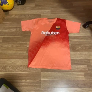 FC Barcelona fotbollströja - Säljer en cool orange FC Barcelona fotbollströja. Tröjan har ett snyggt mönster och klubbens emblem på framsidan. På baksidan finns namnet 'Messi' och nummer 10 i svart. Perfekt för alla Barca-fans! 🔥
