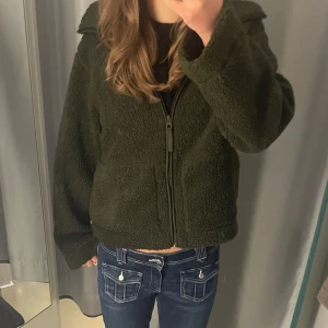 Grön teddyjacka med dragkedja - Mysig grön teddyjacka med dragkedja framtill. Jackan har långa ärmar och en bekväm passform, perfekt för kyligare dagar. Populär pilejacka från hm, i strl xs.