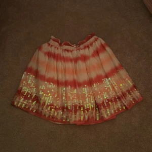 Färgglad kjol med paljetter från H&M - Säljer en färgglad kjol från H&M med ett härligt mönster i orange och rosa nyanser. Kjolen har glittriga paljetter längs nederkanten som ger en festlig touch. Perfekt för att lysa upp garderoben! 💖