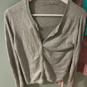 Grå kofta från Zara - Säljer en stilren grå kofta från Zara. Den har en klassisk design med knappar framtill och långa ärmar. Perfekt för lager-på-lager-stil eller som ett lättare ytterplagg.
