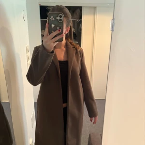 Brun kappa - Snygg brun kappa med klassisk design. Perfekt för höst och vår. Den har en rak passform och långa ärmar, vilket ger en stilren look.