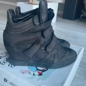 Svarta sneakers med kilklack - Snygga svarta sneakers med kilklack och kardborreband. Perfekta för en stilren look med en twist. Skorna har en rund tå och är tillverkade i syntetmaterial.