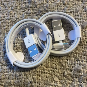 Vita USB-kablar - Två vita USB-kablar med USB-A till USB-C anslutningar. Perfekta för laddning och dataöverföring. Kablarna är snyggt ihoprullade och hålls på plats med vita kabelband.
