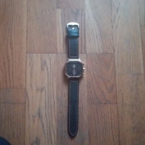 Svart och guld klocka med fyrkantig urtavla Magnus Dagur - Snygg klocka med svart läderarmband och fyrkantig urtavla i guld. Urtavlan har detaljer i svart och guld med flera visare och en datumvisare. Perfekt accessoar för den stilmedvetne.