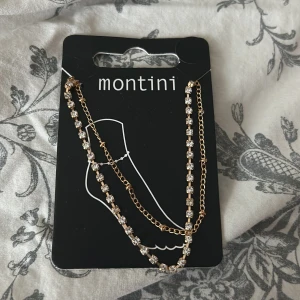 Guldigt fotlänk från Montini - Elegant fotlänk från Montini i guld med glittrande stenar. Perfekt för att ge en extra touch till din outfit. Fotlänken har en kedjedesign med små, gnistrande detaljer som fångar ljuset vackert.