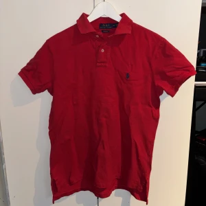 Röd pikétröja från Ralph Lauren - Säljer en klassisk röd pikétröja från Ralph Lauren med korta ärmar och en broderad logotyp på bröstet. Perfekt för en stilren och avslappnad look.