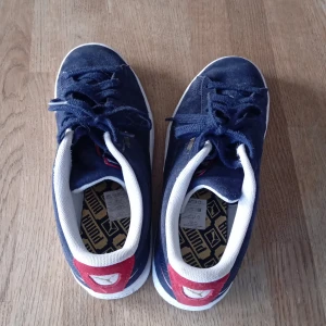 Blå sneakers med röd detalj - Snygga blå sneakers med vit sula och röd detalj på hälen. Skorna har snörning och en rund tå, vilket ger en klassisk look. Perfekta för en avslappnad stil.