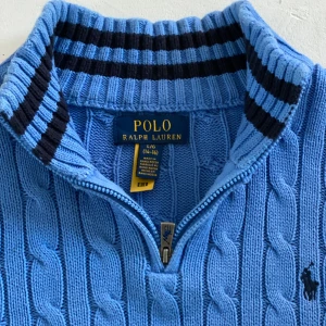 Ralph Lauren Quarter-Zip  - Ralph Lauren kabelstickad quarter-zip – Strl L (14–16 år / 170 cm)  Stilren och klassisk tröja från Ralph Lauren i kabelstickat material med quarter-zip i kragen. Supersnygg till både vardags- och mer uppklädda looks. Knappt använd och i mycket fint skick! 	•	Storlek: L (14–16 år / ca 170 cm) 	•	Modell: Quarter-zip sweater 	•	Färg: [lägg till om du vill – t.ex. marinblå, grå etc.] 	•	Kabelstickad bomull 	•	Original från Ralph Lauren 	•	Väldigt sparsamt använd