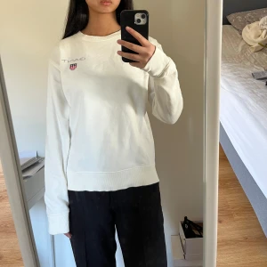 Vit sweatshirt från Gant - Säljer en stilren vit sweatshirt från Gant med deras logga och ett litet emblem på bröstet. Tröjan har långa ärmar och en rund halsringning. Fint skick. Lite längre i armarna och även på längden. Det står 176 cm, 16 years i den som en barnstorlek men det passar en i storlek S. 