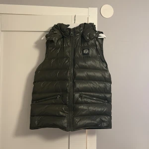 Grön dunväst från Bvaldi - Snygg grön dunväst från Bvaldi med dragkedja och huva. En perfekt väst nu till våren/sommaren! Västen är helt slutsåld på deras hemsidan och kommer nog inte släppas nya på länge. Denna väst är i storlek medium och är använd 1-2 gånger. Ordenarie pris på västen är 1899kr. Eftersom den är slutsåld och eftertraktad så höjs priset därav. Hör av er vid fler frågor och intresse! Pris går att diskuteras. Kvitto finns, 