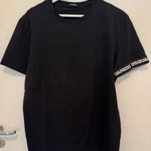 Svart t-shirt från Dsquared2 - Snygg svart t-shirt från Dsquared2 med logga på ärmen. Tillverkad i mjuk bomull med lite stretch för extra komfort. Perfekt för en stilren look.