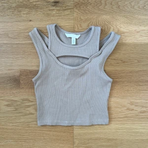 Linnetopp - Säljer en stilren beige ribbad linnetopp från H&M. Toppen har en unik design med ett snyggt utskuret parti framtill. Perfekt för varma dagar eller som ett lager under en jacka. Använd en gång 🩷