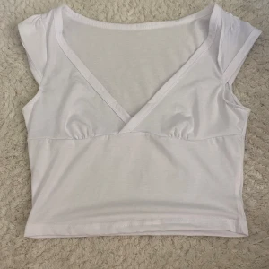Vit croppad v-ringad topp - Säljer en vit croppad topp med v-ringning och korta ärmar. Toppen har en enkel och stilren design, perfekt att matcha med jeans eller kjol. Mjuk och skön i bomullsmaterial, passar dig som gillar en clean och fräsch look.