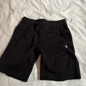 Svarta shorts Polo Ralph Lauren - Svarta shorts från Polo Ralph Lauren med klassisk logga broderad på benet. Modellen har snörning i midjan, fickor fram och en bakficka. Slim fit och tillverkade i mjuk bomull, perfekta för chill dagar eller när du vill ha en clean look.