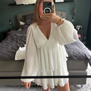 Vit omlottklänning från Nelly - Superfin vit kortklänning från Nelly med v-ringning, omlottkänsla och långa puffärmar. Klänningen har plisserat tyg och volangdetaljer som ger en flowy look. Perfekt för dig som gillar romantisk och trendig stil.