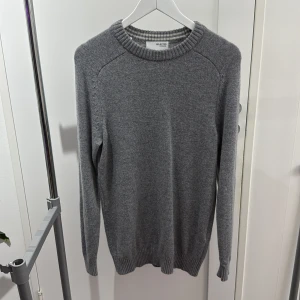 Grå stickad tröja från Selected Homme - En klassisk grå stickad tröja från Selected Homme i storlek XS. Tröjan har rund halsringning med ribbade muddar vid hals, ärmslut och nederkant. Perfekt för lager-på-lager och enkel att matcha med jeans eller chinos. Tröjan är som sagt i XS men kan också bäras om du har str S 
