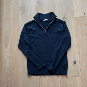 Mörkblå halvziptröja i merinoull - Mörkblå stickad tröja i 100% merinoull från C. Tröjan har en ribbad hög krage och en snygg half zip-dragkedja framtill. Perfekt för lager-på-lager och chill stil. Långärmad och med ribbade muddar för extra komfort. Priset får gärn diskuteras
