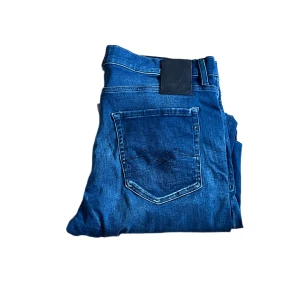 Replay Hyperflex jeans  - Säljer ett par Replay Hyperflex jeans i klassisk blå tvätt. Jeansen har raka ben, fem fickor och snygga slitningar. Materialet är stretchigt för extra komfort och passformen är normal. Perfekta för dig som gillar stilrena och bekväma jeans. Längd ca 112cm. Jag skickar ej bild när jag bär plaggen och jag vet ej vilken längd och vikt de passar då jag inte prövar kläderna jag säljer, så för storlek hänvisar jag till måtten och passform att man googlar på modellnamn etc 😃