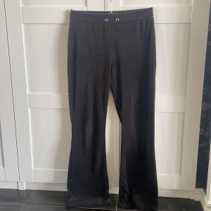 Svarta bootcut byxor i mjukis - Svarta mjukisbyxor med bootcut passform och två bakfickor. Byxorna har resår i midjan med metallöljetter framtill och är gjorda i ett mjukt, stretchigt material som känns riktigt skönt mot huden.