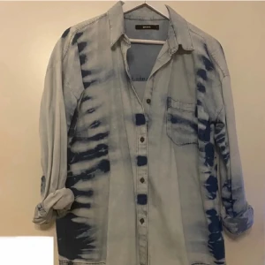 jeansskjorta - Säljer en snygg jeansskjorta från Bik Bok i ljusblå denim med mörkblå skuggdetaljer – en riktigt trendig design! 📏 Storlek: S, men modellen är lite oversize så den passar även M eller L 🧼 Använd endast 2–3 gånger, i nästan nyskick – inga skador eller slitage