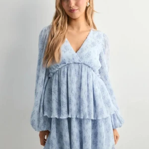 Ljusblå blommig kortklänning med volang - Superfin ljusblå kortklänning med blommigt mönster och v-ringning. Klänningen har långa, luftiga ärmar och volangdetaljer i midjan och nederkant. Perfekt flowy passform och lätt, skir känsla. Bara använd en gång💗